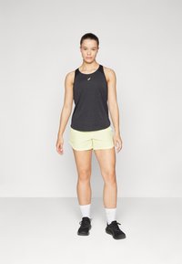 Black sleeveless athletic top with light reflective logo, paired with bright yellow shorts. Model wears black sneakers and white socks.