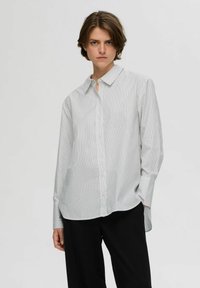 Camicia con bottoni di colore grigio chiaro con sottili strisce verticali, maniche lunghe, colletto e una vestibilità rilassata. Il tessuto appare liscio e leggero.