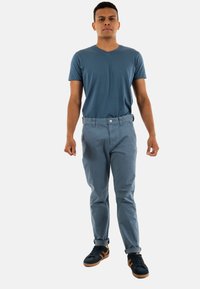 Conjunto casual de hombre que presenta una camiseta de cuello en V azul y pantalones azul claro, con zapatillas negras y puños enrollados.