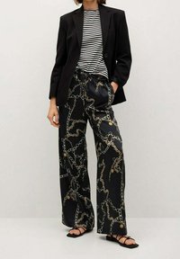 Blazer noir, t-shirt à rayures et pantalon à jambes larges avec un motif de chaîne dorée. Le pantalon présente une taille élastique et une texture lisse et brillante.