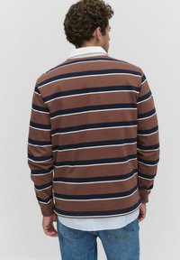 Long-sleeve, brown-striped shirt featuring navy and white horizontal stripes, with a white collar and a layered hem above denim pants.