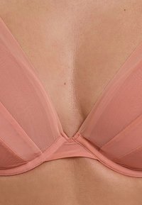 Soutien-gorge en mesh rose avec un décolleté plongeant et de douces bonnets en forme de triangle. Présente un design sans couture et des coutures subtiles le long des bords.