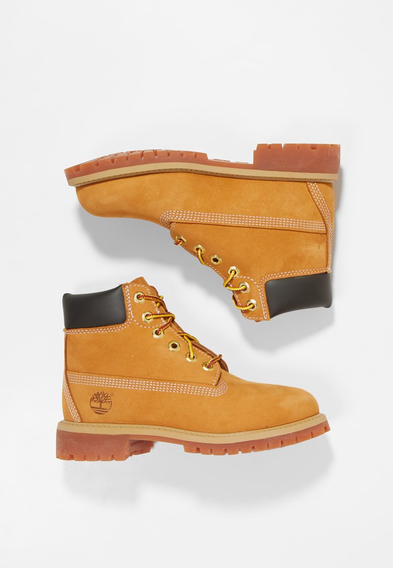 Stivaletti alla caviglia in suede beige con lacci gialli, suole in gomma marrone e tacco in pelle nera. Presentano cuciture bianche e un logo stampato sul lato.