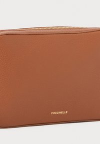 Brun læderpung med en struktureret overflade, guld lynlås og præget mærkenavn "COCCINELLE" i nederste højre hjørne.