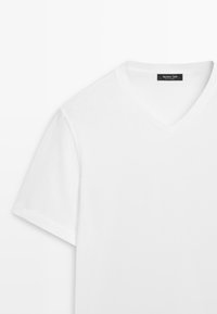 T-shirt blanc à col en V et manches courtes, avec une étiquette de vêtement noire à l'intérieur du col portant l'inscription « Massimo Dutti ».