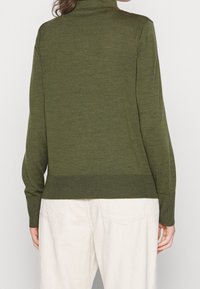 Olive green turtleneck sweater made of soft knit fabric, featuring long sleeves and a ribbed hem, paired with light-colored corduroy pants.