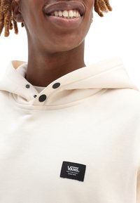White hooded sweatshirt with a textured finish, featuring a black VANS logo patch and button accents near the neckline.