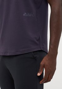 T-shirt en coton violet avec un col rond, des manches courtes et un détail imprimé près de l'ourlet. Assorti avec un pantalon noir.