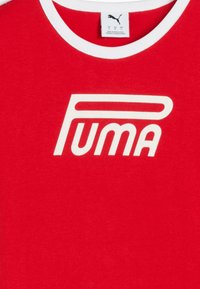 Röd bomullen t-shirt med vit rund halsringning och djärv vit "Puma" logotyp över bröstet. Tyget verkar slätt och lätt.