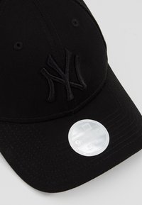 Casquette de baseball noire avec logo NY en relief et un autocollant 9FORTY blanc et ajustable sur la visière sur fond clair.