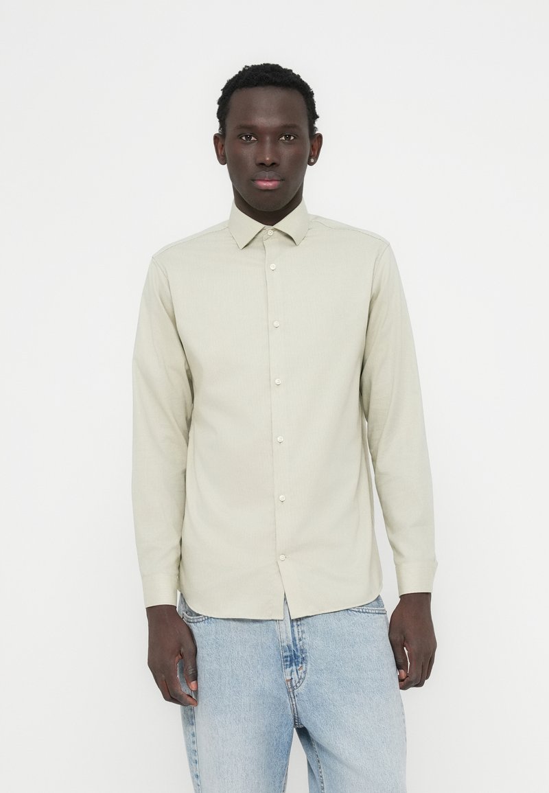 Μακρυμάνικο πουκάμισο ανοιχτό πράσινο με γιακά με κουμπιά, διαθέτει λεπτή υφή και κλείσιμο με κουμπιά στο εμπρός μέρος, συνδυασμένο με μπλε τζιν παντελόνι.