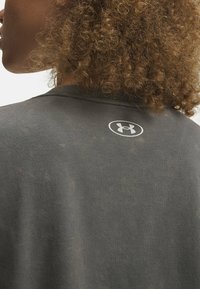 Tmavosivá tričko s jemnou textúrou, na hornej časti chrbta je malé biele logo Under Armour. Jednoduchý dizajn s okrúhlym výstrihom.