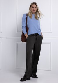 Lichtblauwe geribbelde trui, donkergrijze broek met losse pasvorm en trekkkoord in de taille, glanzende zwarte schoenen. Bruine schoudertas hangt aan de linkerschouder.