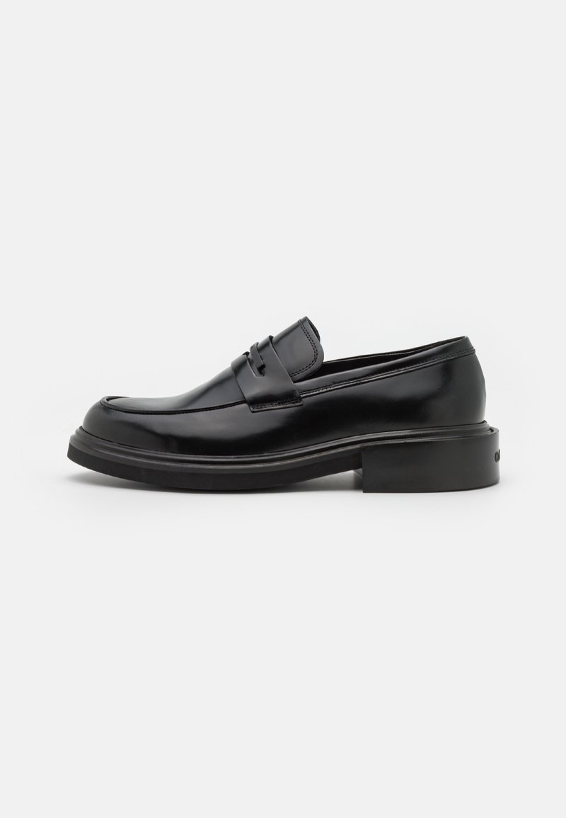 Mocassin en cuir noir avec un bout arrondi, bande décorative à l'avant et un petit talon rectangulaire. Fini lisse et détail minimal.