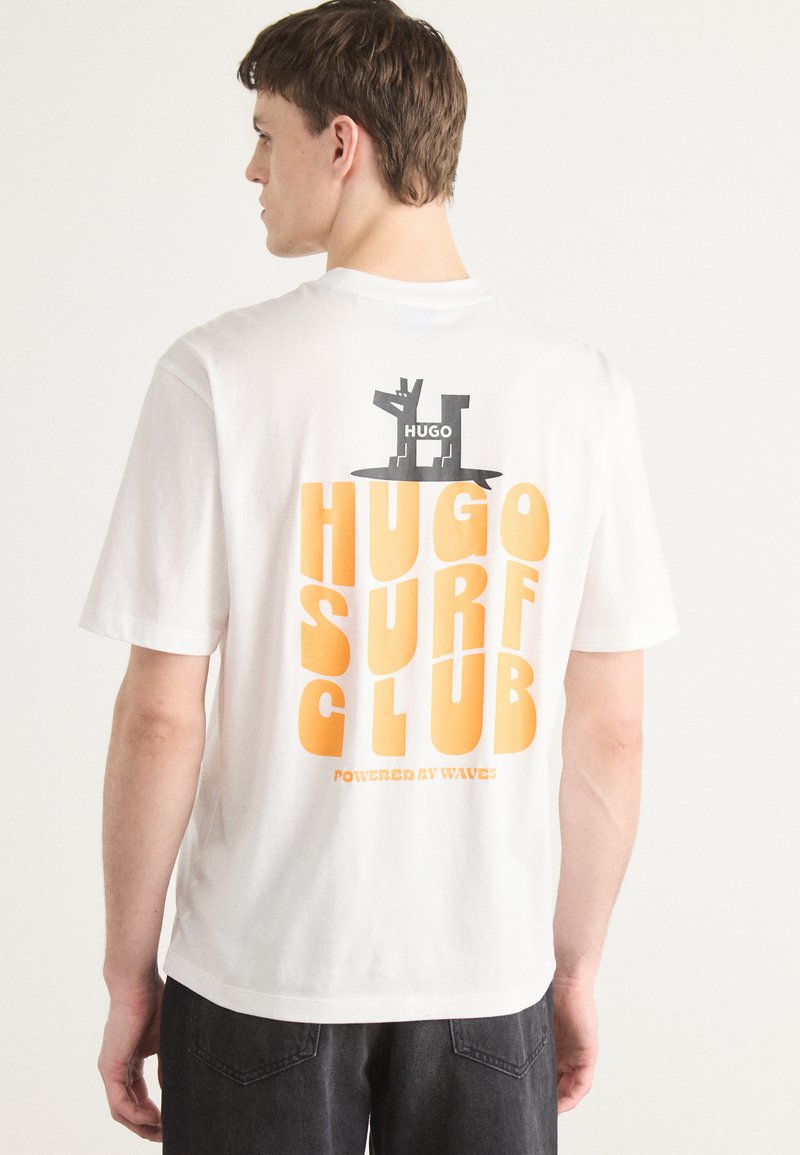 T-shirt en coton blanc avec un texte graphique orange audacieux indiquant "HUGO SURF CLUB" et un petit logo noir au dos.