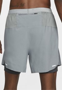 Vue de dos d'une personne portant un short de course Nike gris clair avec une doublure intérieure noire et une poche zippée à la ceinture.