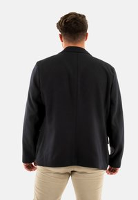 Blazer blu navy con un design strutturato, caratterizzato da maniche lunghe, rever a scollatura e un taglio dritto. Tessuto testurizzato con linee minimaliste.