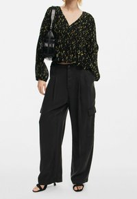Blouse noire à fleurs avec manches longues et col en V, portée avec un pantalon cargo noir ample avec poches latérales. Sandales noires à lanières et sac à main.