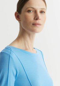 Jasnoniebieska bluzka z okrągłym dekoltem i długimi rękawami. Posiada gładką teksturę i kontrastowe wykończenie szwów na ramionach.