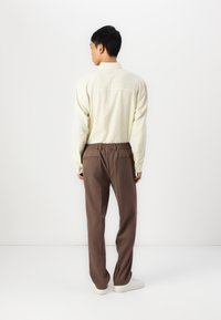 Light yellow button-up shirt with a textured weave, paired with brown trousers featuring an elastic waistband and back pockets.