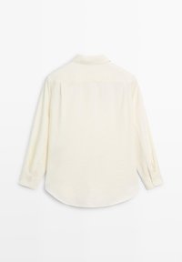 Camicia beige chiaro a maniche lunghe con colletto abbottonato, tessuto liscio e orlo arrotondato. Presenta un unico pettorale posteriore e bottoni sulle maniche.