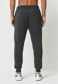Dunkelgraue Sweatpants mit einer schmal zulaufenden Passform, elastischem Bund und einer kleinen Gesäßtasche, kombiniert mit sportlichen weißen und blauen Schuhen.