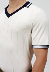 Camisa polo de punto crema de manga corta con cuello y puños a rayas marino, que presenta una textura acanalada vertical y un diseño de escote en V.