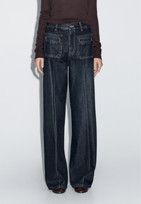 Dark wash wide-leg jeans with a high waist, featuring two back pockets, side seams, and contrast stitching. Made of denim fabric.