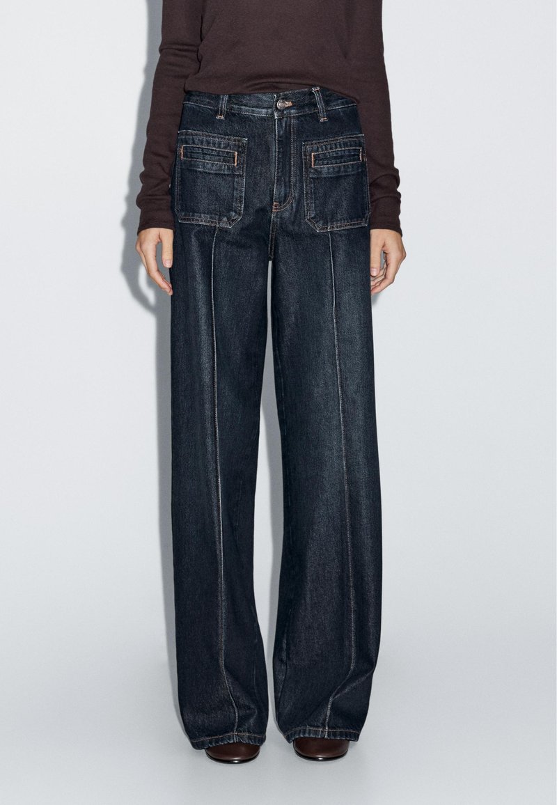 Dark wash wide-leg jeans with a high waist, featuring two back pockets, side seams, and contrast stitching. Made of denim fabric.