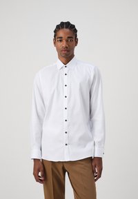 Fehér hosszúujjú ing fekete gombokkal, gombnyomott gallérral és egységes gombos mandzsettákkal. Simaságú pamut anyag, testhezálló design.