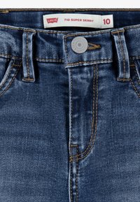 Levi's 710 Super Skinny džínsy v tmavomodrom denime, s hladkou textúrou, medeným prešívaním a strieborným gombíkom na zapínanie v páse.