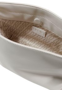 Bolso de cuero sintético color crema con exterior liso y forro de patrón geométrico. Cuenta con cierre de presión y etiqueta de la marca en el interior.