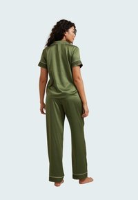 Set di pigiami in satin verde caratterizzato da una maglietta a maniche corte con piping bianco e pantaloni lunghi con polsini texturizzati. Tessuto liscio e morbido.
