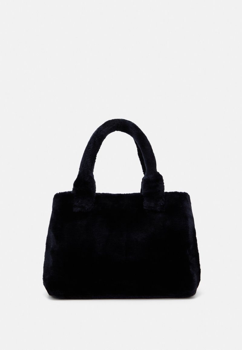 Sac à main en fausse fourrure noire douce avec poignées doubles arrondies et corps rectangulaire sur fond gris clair uni.