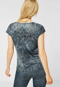 Kortärmad, blågrå t-shirt med en texturerad, mönstrad design. Bakdelen har en rund halsringning och en något lös passform.