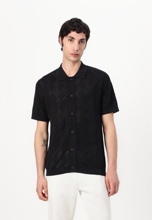 Schwarzes kurzärmliges Strickpolohemd mit diamantförmiger Netzstruktur und einem einfarbigen Kragen, der mit Knöpfen vorne geschlossen ist.