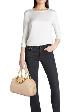 Borsa beige con superficie texturizzata, manico a catena dorata e chiusura con zip, abbinata a una maglietta bianca e jeans neri.