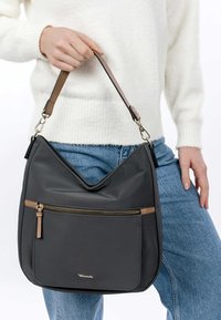 Szara nylonowa torba na ramię z otworem w kształcie litery V, brązowymi skórzanymi akcentami i zapinaną na zamek przednią kieszenią. Gładka tekstura, casualowy design.