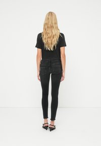 Μαύρο βαμβακερό μπλουζάκι σε συνδυασμό με σκούρο στενό τζιν με ξεφτισμένο τελείωμα. Τα παπούτσια είναι μαύρα σανδάλια με τακούνι. Θέα από πίσω.