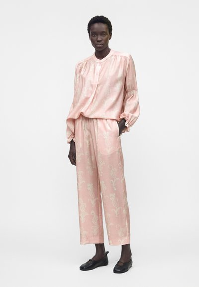 Γυναίκα που φοράει φαρδιά ανοιχτό ροζ μπλούζα και αντίστοιχο πλατύ παντελόνι με ανοιχτό λουλουδάτο μοτίβο, συνδυασμένο με μαύρα πλατφόρμα παπούτσια.
