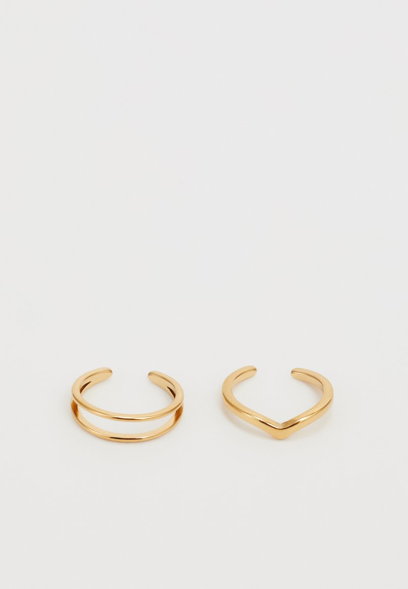 Gold-colored metal rings, one with a double band design and the other featuring a V-shape. Smooth texture, minimalist design.