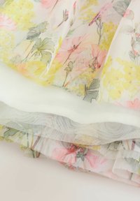 Kvetinová tylová látka s pastelovými ružovými, žltými a zelenými vzormi; vrstvená s jemnou bielou podšívkou; priehľadná textúra s jemnými detailmi.