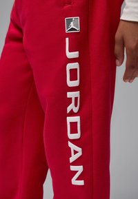 Punased dressipüksid valge "JORDAN" kirjaga ja musta logomärgiga, millel on hüppav figuur. Pehme tekstuur ja kitsenev lõige.