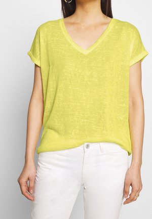 Haut jaune vif à manches courtes et col en V, fabriqué dans un tissu léger et texturé, avec une coupe décontractée. Porté avec un pantalon blanc.