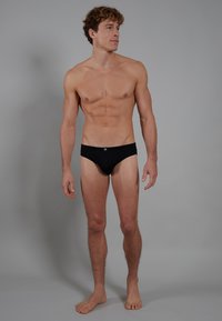 Caleçons de bain noirs en tissu lisse, avec une coupe ajustée, une taille basse et une marque minimale à l'avant.