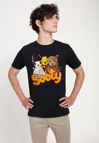Svart T-shirt med färgglada plyschkaraktärer och ordet "Sooty" i fet, gul skrift. Kort ärm och rundad halsdesign.