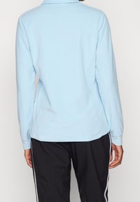 Polo de manga larga azul claro con dobladillo recto y textura sutil. Combinado con pantalones negros con rayas laterales blancas.