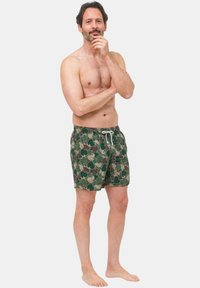 Costumi da bagno da uomo in verde con un motivo giocoso di scimmie. Presentano una vita elastica con un cordino bianco per una vestibilità regolabile.