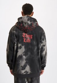Felpa con cappuccio con motivo tie-dye nei colori grigio e nero. Sul retro è presente la scritta "Thug Life" in lettere rosse con accenti di design.