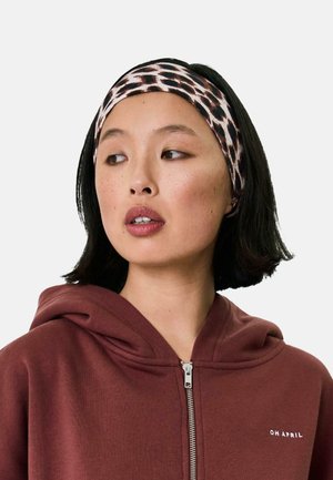 Leopardenmuster-Haarband aus dehnbarem Stoff, das ein helles und dunkles Farbenspiel aufweist und mit einem burgunderfarbenen Reißverschluss-Hoody getragen wird.